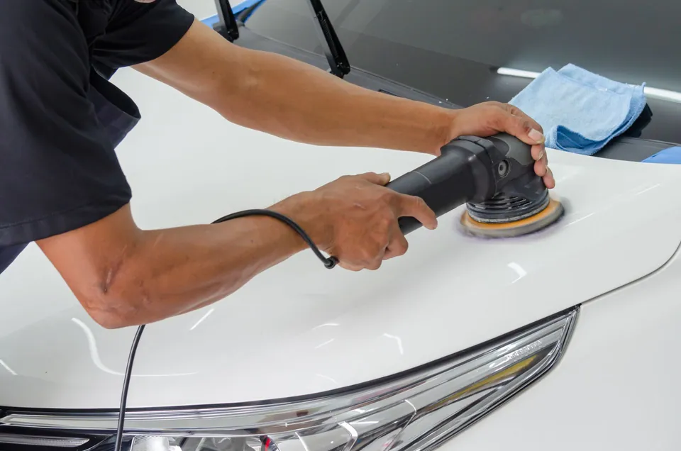 Detailer using a polisher on a white car hood